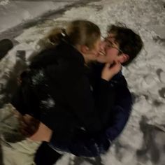 two people sitting in the snow kissing each other