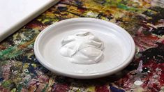 a white bowl filled with whipped cream sitting on top of a colorful painting tablecloth