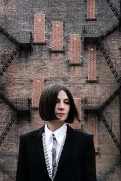 a woman wearing a suit and tie standing in front of a brick wall with iron bars