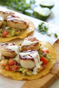 two tacos with shrimp and guacamole on them sitting on a cutting board