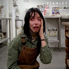 a woman holding her head in front of her face while standing in a kitchen area