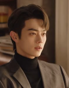 the young man is wearing a suit and black turtle neck sweater, looking off into the distance