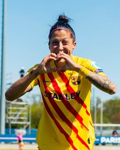 a female soccer player in yellow and red uniform making a heart shape with her hands