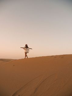 a woman standing on top of a sand dune in the desert with her arms outstretched