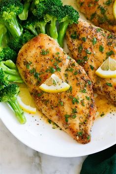 two pieces of chicken on a plate with broccoli and lemons next to it