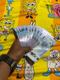 a person is holding up some money on a yellow and orange blanket with cartoon characters