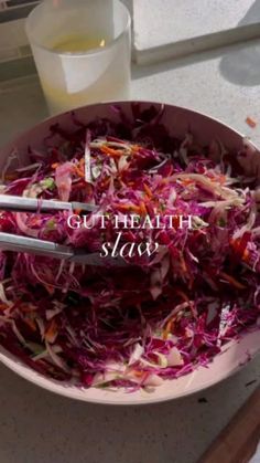 a bowl filled with shredded red cabbage next to a glass of water and spoons