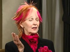 a woman with red hair and pink flowers in her lap is talking to the camera