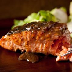 a piece of meat with sauce on it next to some vegetables and a fork in the foreground