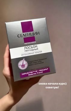 a hand holding up a box of cosmetic product in front of a wall with the words ceafhilh on it