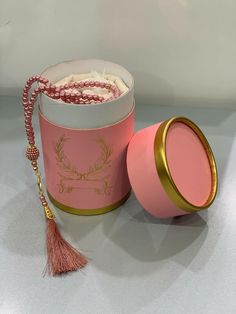 a pink and gold canister with a tassel in it sitting on a table