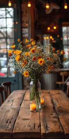 a vase filled with yellow flowers sitting on top of a wooden table next to candles