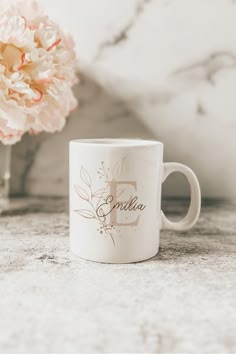 a white coffee mug sitting next to a pink flower