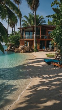 a house on the beach surrounded by palm trees and blue water with lounge chairs in front