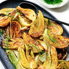 a black plate topped with roasted artichokes next to a bowl of sauce