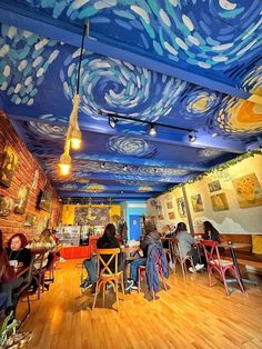 people are sitting at tables in a room with painted ceilings and wooden floors, while the ceiling is decorated with blue swirls