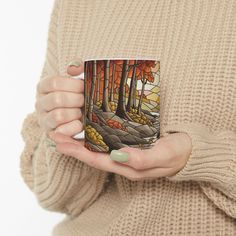 a woman is holding a coffee mug in her hands with trees and rocks painted on it