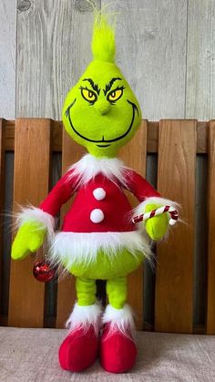 the grinch is holding a candy cane in his hand and standing next to a wooden fence