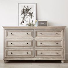 a white dresser with drawers and pictures on top