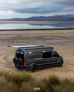 a van parked in the middle of a field with water and mountains in the background