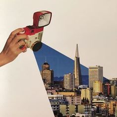 a hand holding a red and white camera over a city