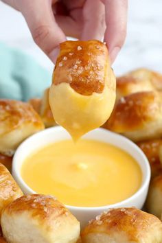 a person dipping some bread into a small bowl with butter on the side and other rolls in the background