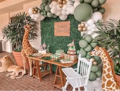 two giraffes are standing in front of a table with balloons and greenery