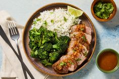 a plate filled with meat, rice and broccoli next to two bowls of sauce