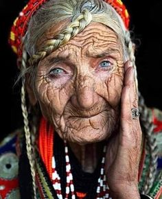 an old woman with wrinkles and braids holding her hands up to her face