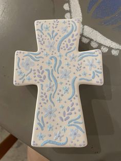 a ceramic cross with blue and white designs on it sitting on a glass table top