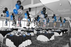 a room filled with tables covered in black and white table cloths, blue and silver balloons hanging from the ceiling