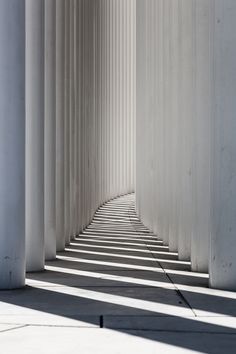 an empty hallway with white columns and shadows on the floor in front of one another