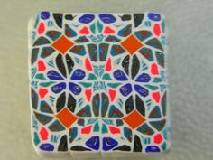 a small square tile with multicolored designs on the outside and inside, sitting on a white surface