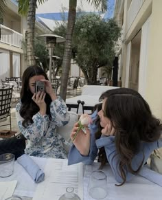 two women sitting at a table taking pictures with their cell phones