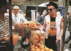 a man standing next to a blender filled with oranges