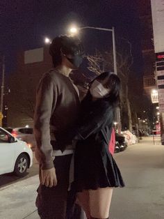 a man and woman standing next to each other on the street at night with their faces covered by masks