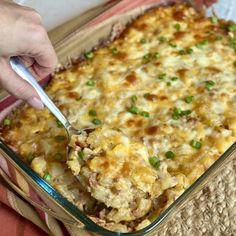 a person holding a spoon in a casserole dish with green onions and cheese