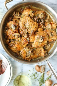 chicken with mushrooms and sauce in a pan on a marble countertop next to silver utensils