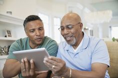 two men sitting on a couch looking at an electronic tablet computer screen while they look at it