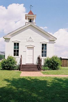 a small white church with a steeple on top and stairs leading up to the door