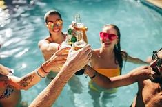 group of people in swimming pool holding up bottles of beer to take pictures with cameraman