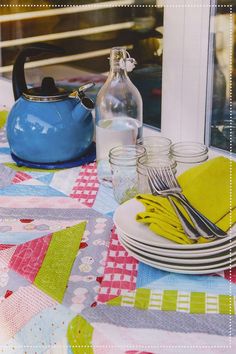 the table is set with plates, silverware and a blue teapot on it