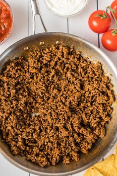 a skillet filled with ground beef next to tortilla chips and tomatoes