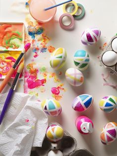 an assortment of painted eggs on a table with paintbrushes and other items nearby