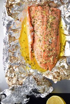 a piece of salmon on tin foil with lemon wedges and seasoning next to it