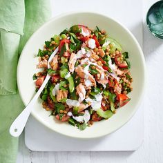 a white plate topped with a salad next to a green napkin and fork on top of a cutting board