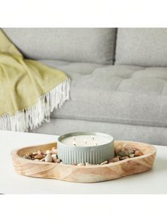 a white candle sitting on top of a wooden tray filled with rocks and gravel next to a gray couch