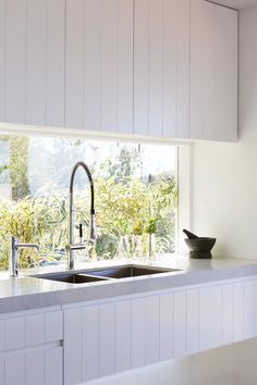 a kitchen with white cabinets and a sink in front of a window that looks out onto the outdoors