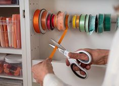 a person holding scissors in front of a shelf with many different colored ribbons on it