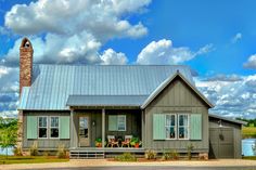 a gray house with green shutters on the front and side windows, sitting under a cloudy blue sky